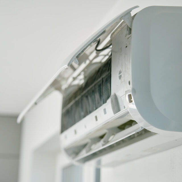 White air conditioner unit is mounted on wall, ready for maintenance. Climate system with opened front cover revealing internal components. Repairing HVAC in apartment